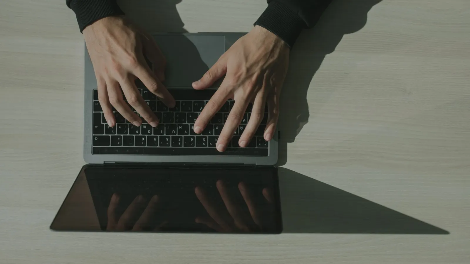 Tangan mengetik di laptop di atas meja kayu terang