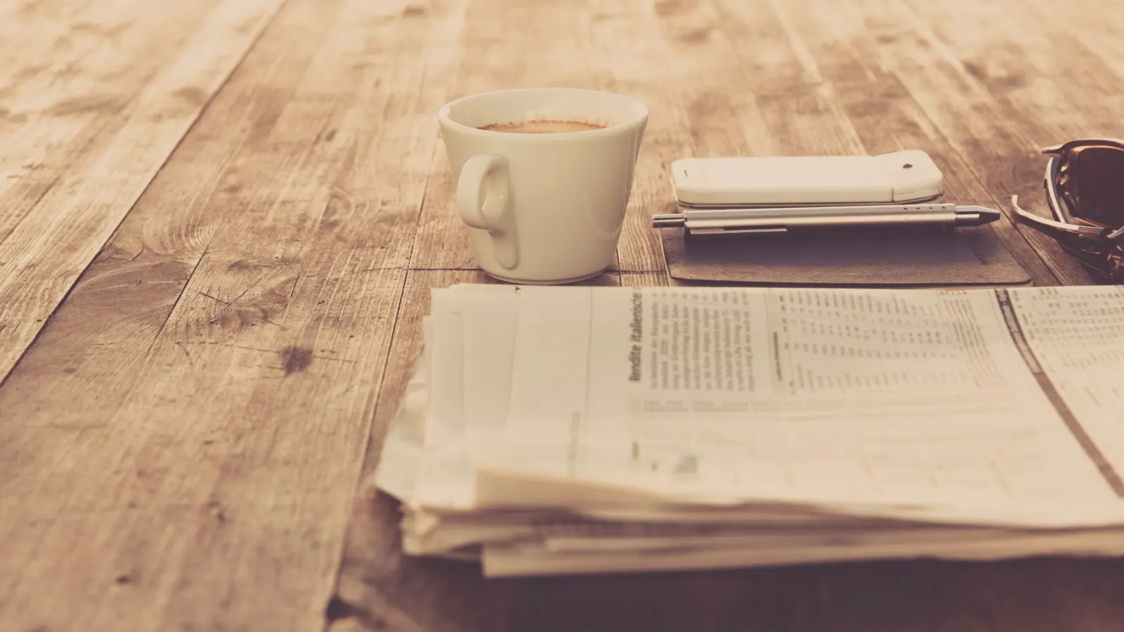 Koran, ponsel, dan cangkir kopi di meja kayu